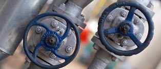 Close-up of two industrial valves with blue handwheels. The valves appear to be part of a piping system, with details of their mechanism visible. The surrounding environment suggests an industrial setting.